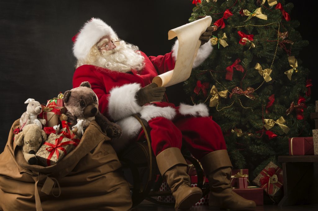 Portrait of happy Santa Claus reading Christmas letter or wish l